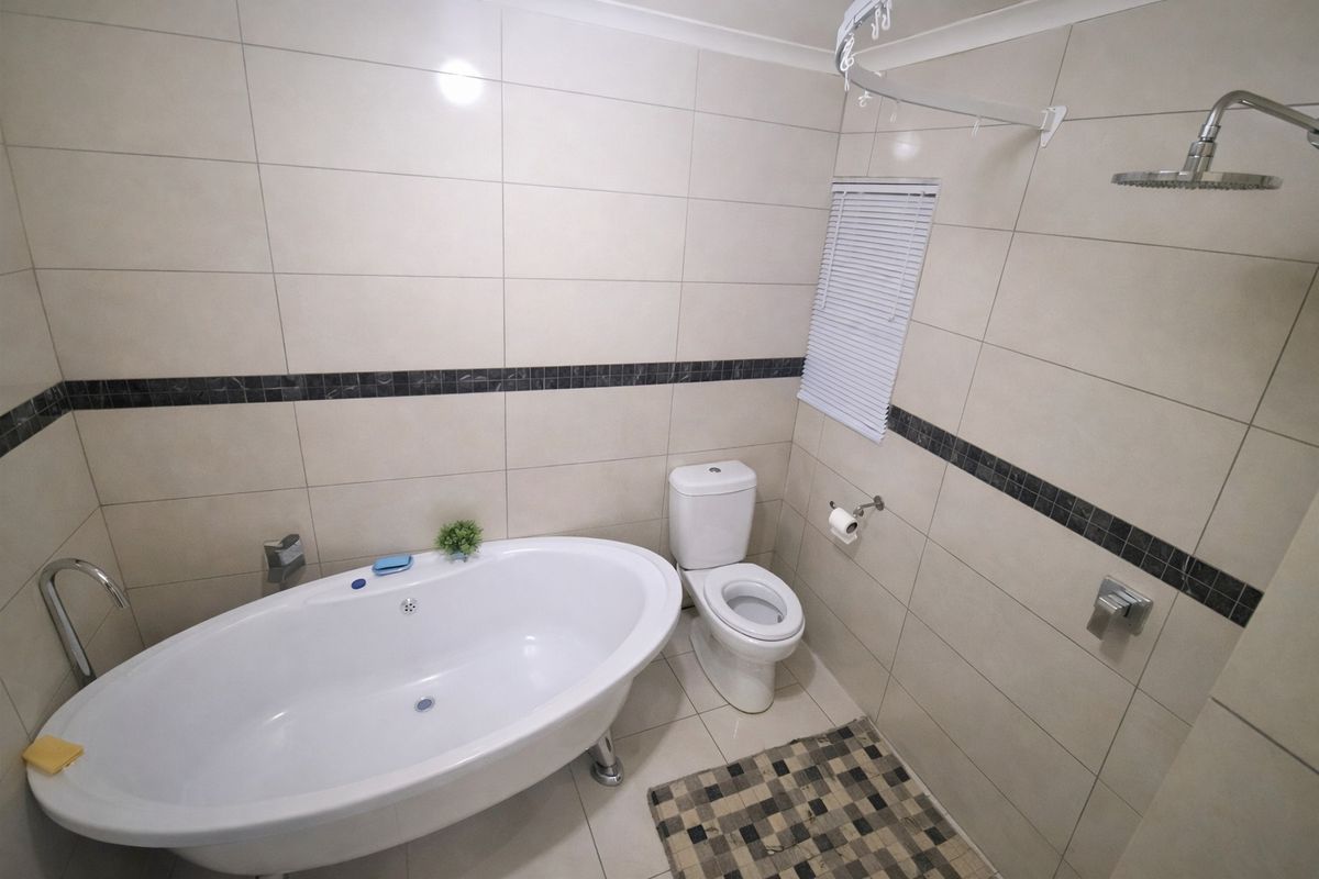 Modern bathroom featuring a freestanding bathtub, a separate rain shower, and neutral wall tiling with a decorative mosaic accent border.