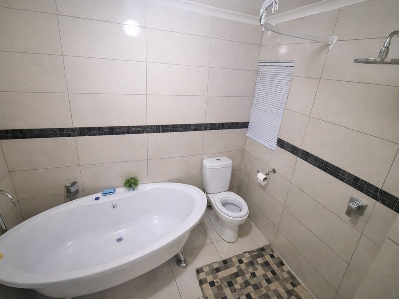 Modern bathroom featuring a freestanding bathtub, a separate rain shower, and neutral wall tiling with a decorative mosaic accent border.