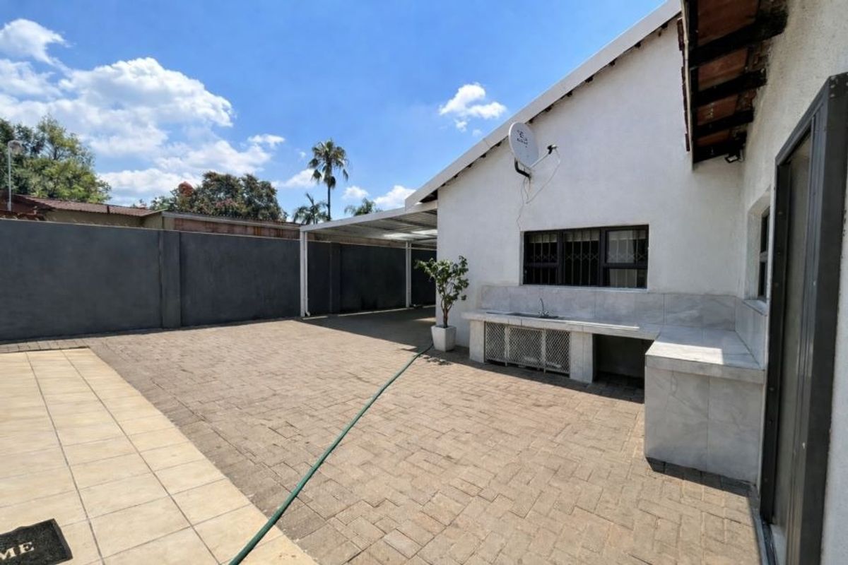 Rear exterior area featuring a paved courtyard, built-in outdoor sink with stone counter, and a covered carport structure.