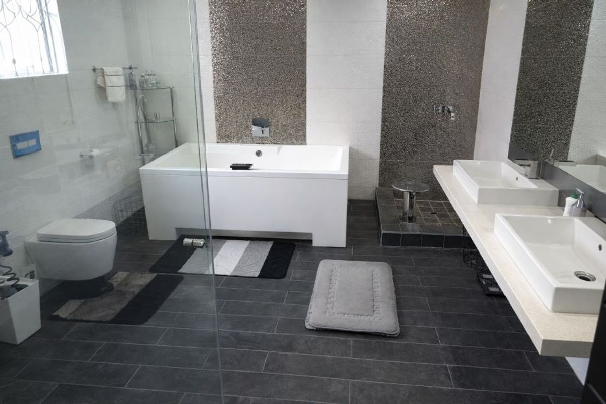 Modern bathroom featuring a double vanity, built-in bathtub, wall-mounted toilet, and a striking mosaic tile feature wall with dark floor tiling.