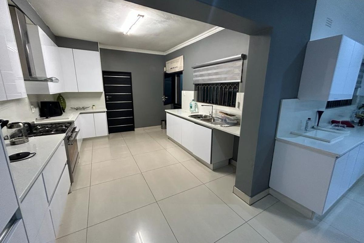 Modern kitchen featuring white cabinetry, stone countertops, gas hob, extractor fan, and tiled flooring in an open-plan layout.