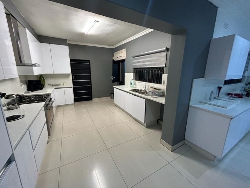 Modern kitchen featuring white cabinetry, stone countertops, gas hob, extractor fan, and tiled flooring in an open-plan layout.