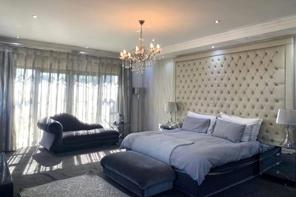 Spacious bedroom featuring a large tufted headboard, elegant crystal chandelier, recessed lighting, and sliding glass doors leading to the exterior.