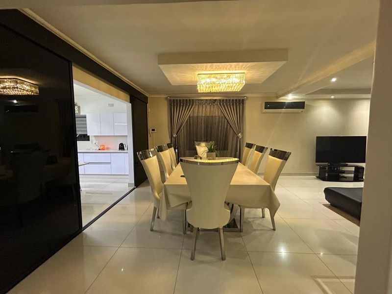 Spacious open-plan dining and living area featuring polished tiled floors, a decorative recessed ceiling with chandelier, and seamless access to the modern kitchen.