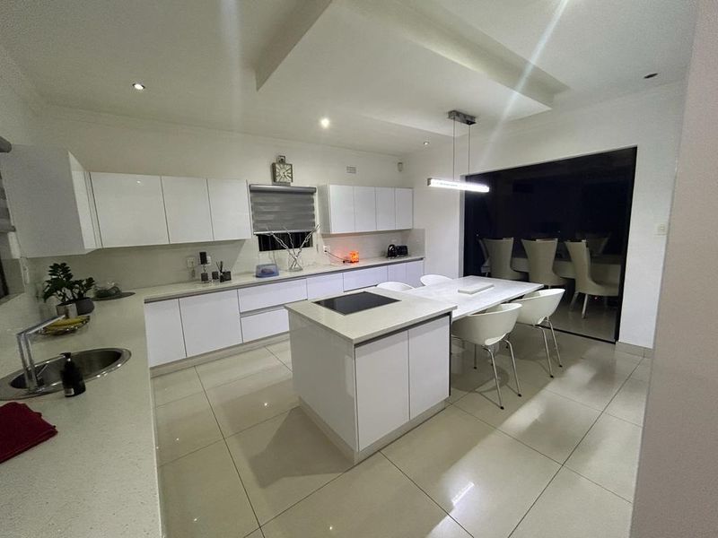 Modern kitchen featuring white cabinetry, stone countertops, a central island with an integrated hob, and sleek tiled flooring with recessed lighting.