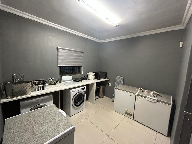 Functional laundry room featuring tiled flooring, built-in countertop space, and dedicated areas for washing machines and chest freezers.