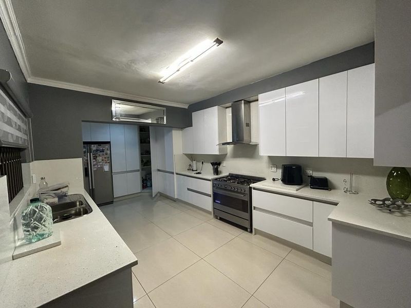 Modern kitchen featuring white gloss cabinetry, stone countertops, stainless steel gas stove, and a convenient walk-in pantry with tiled flooring throughout.