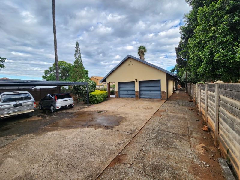 Front exterior view featuring a double garage, a covered carport, and a concrete driveway enclosed by a precast boundary wall.