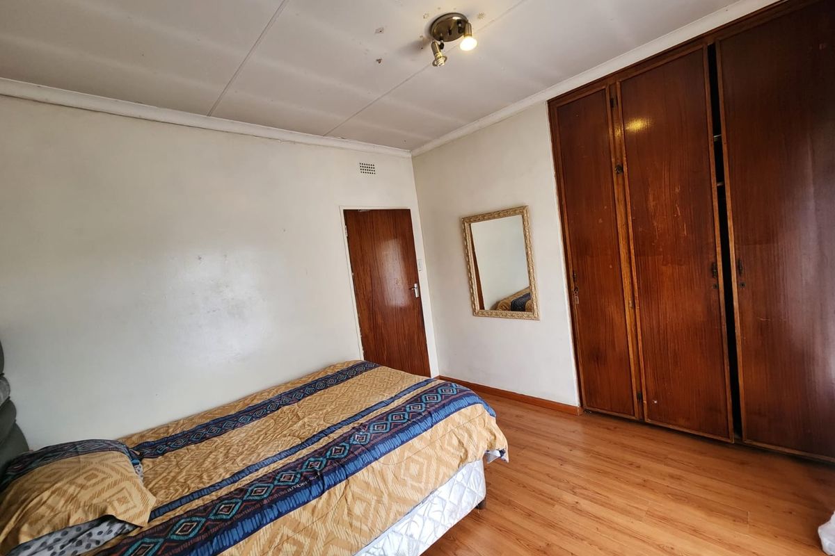 A bedroom featuring laminate flooring and built-in wooden cupboards, showing signs of wear on the ceiling.