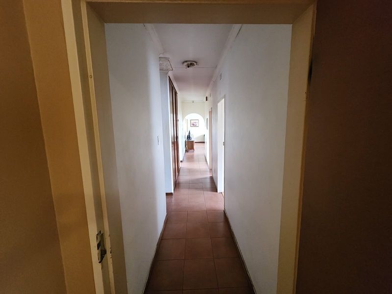 A long, tiled hallway featuring built-in storage cupboards and an arched transition, providing access to various rooms within the home.