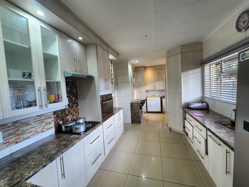 A functional kitchen featuring light-toned cabinetry, dark laminate countertops, a mosaic backsplash, and integrated appliances with tiled flooring throughout.