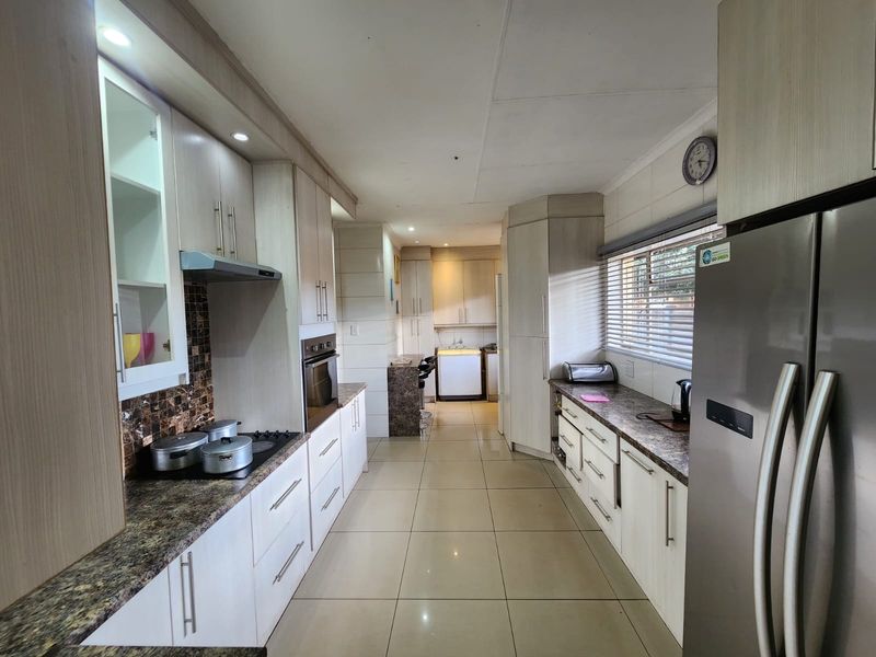 A functional kitchen featuring light-toned cabinetry, granite-look laminate countertops, built-in oven and hob, and tiled flooring with a separate scullery area.