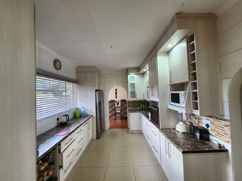 A functional galley-style kitchen featuring light-toned built-in cabinetry, laminate countertops, a built-in oven, and tiled flooring with a view through to the dining area.