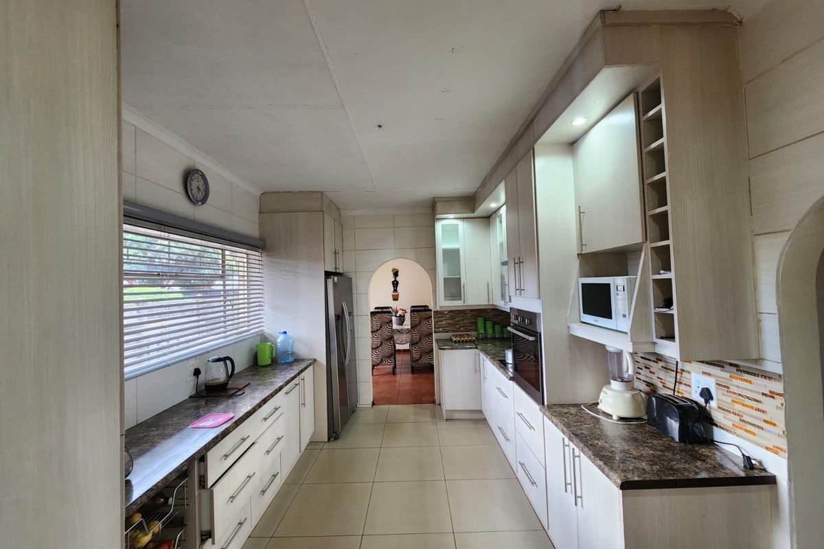 A functional galley-style kitchen featuring light-toned built-in cabinetry, laminate countertops, a built-in oven, and tiled flooring with a view through to the dining area.