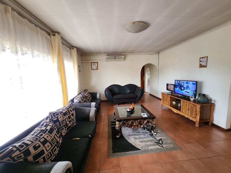 A spacious living room featuring tiled flooring, an air conditioning unit, and a classic archway leading to the rest of the home.