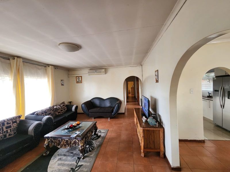 Spacious living room featuring tiled flooring, arched doorways, and a wall-mounted air conditioning unit, offering a functional layout with potential for modernization.