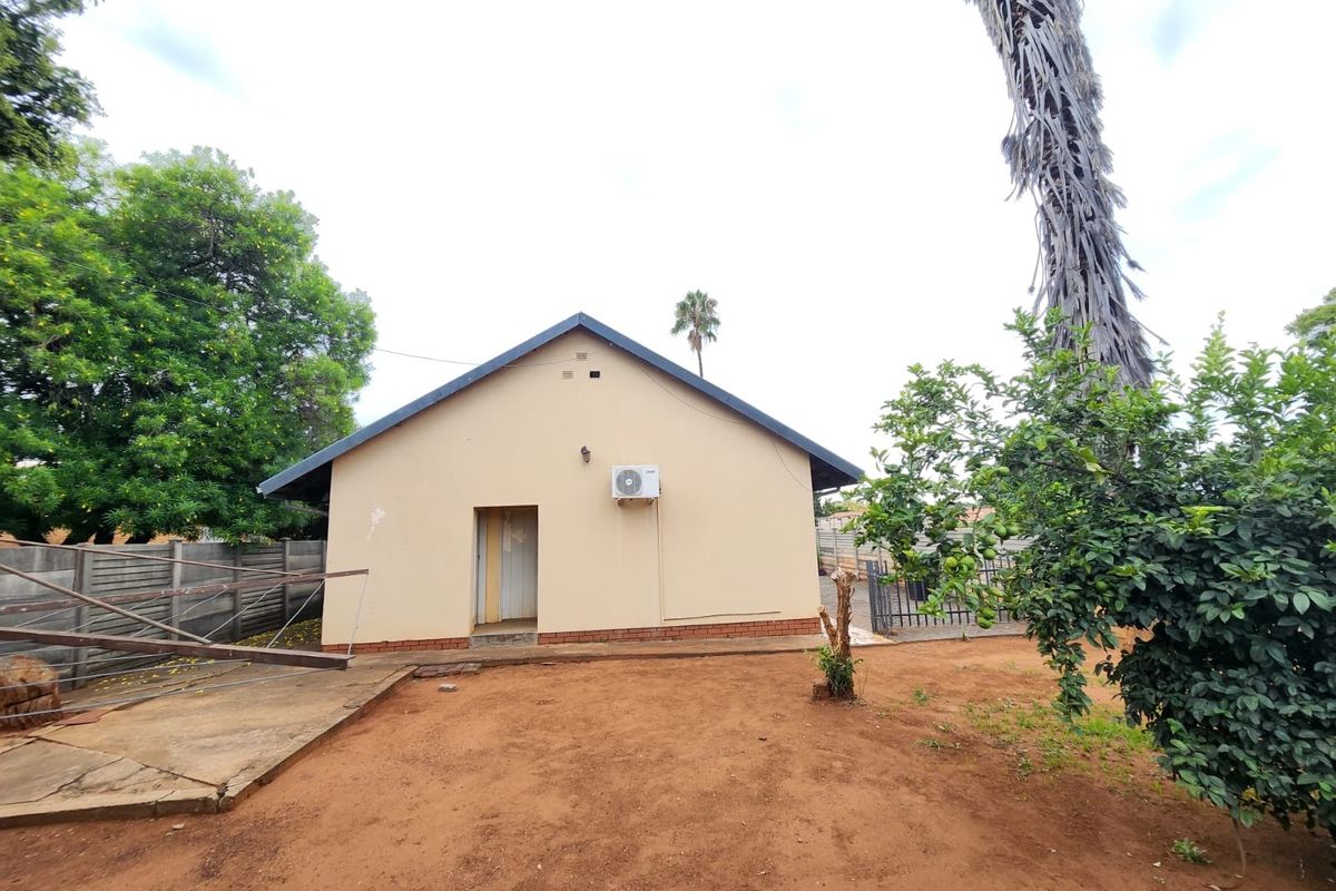 Rear view of the property showing a simple facade, an installed air conditioning unit, and a surrounding garden area with a concrete apron.