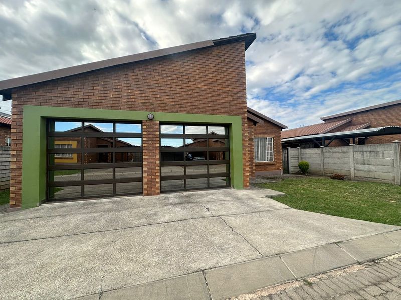Front view of a brick-faced house featuring a double garage with modern metal doors and a concrete driveway.