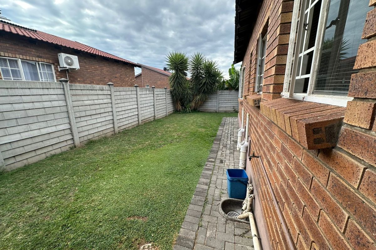 A side view of the property featuring a face brick exterior, paved walkway, lawn area, and precast concrete boundary wall.