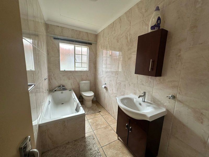 A functional bathroom featuring tiled walls and flooring, a built-in bathtub, a toilet, and a vanity cabinet with a washbasin.