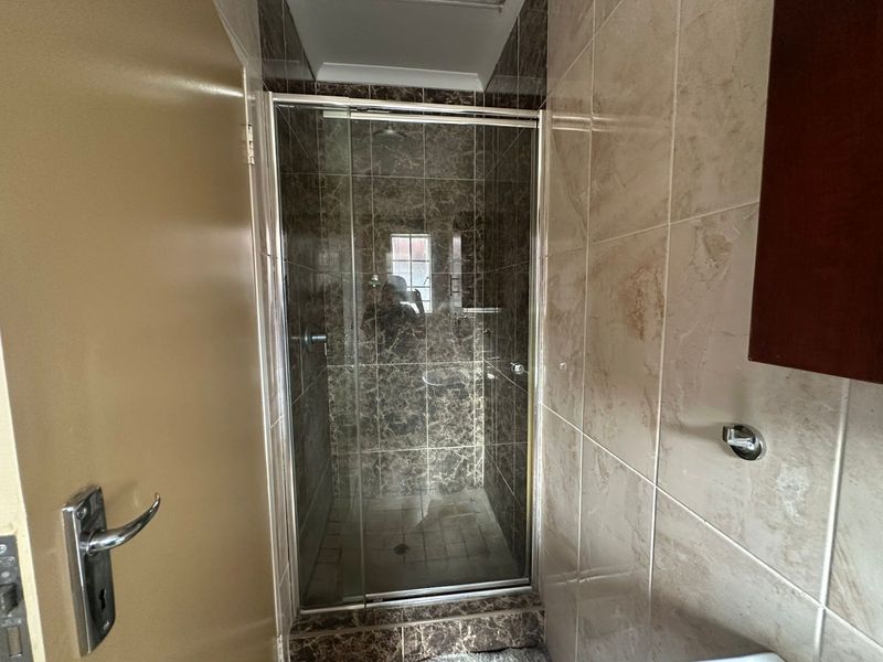 A compact bathroom featuring a glass-enclosed shower with dark marble-effect wall tiles and neutral floor tiling.