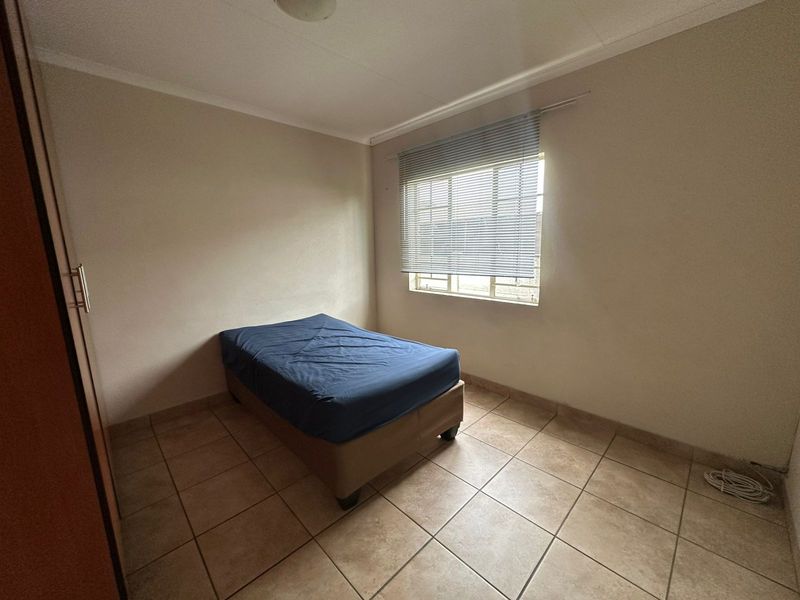 A simple bedroom featuring tiled flooring, a built-in cupboard, and a window fitted with a venetian blind.