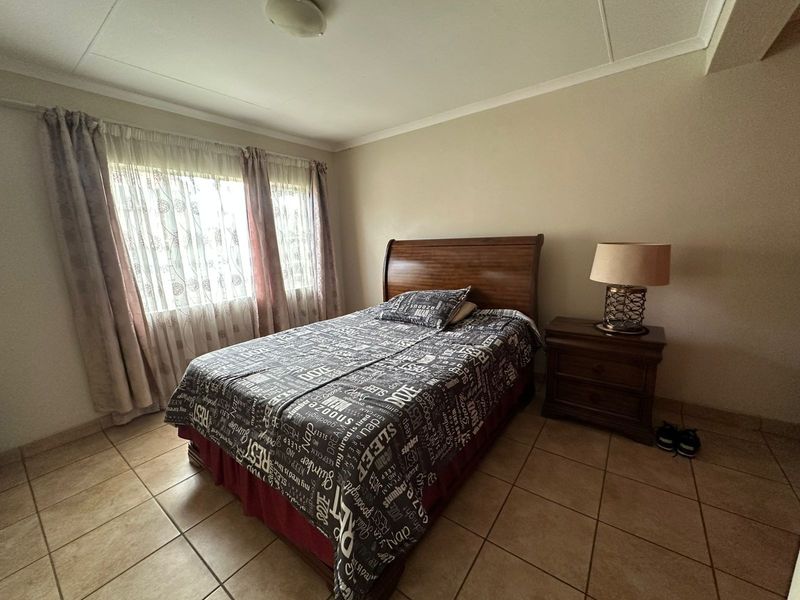 A functional bedroom featuring tiled flooring, neutral wall finishes, and natural light through large windows.