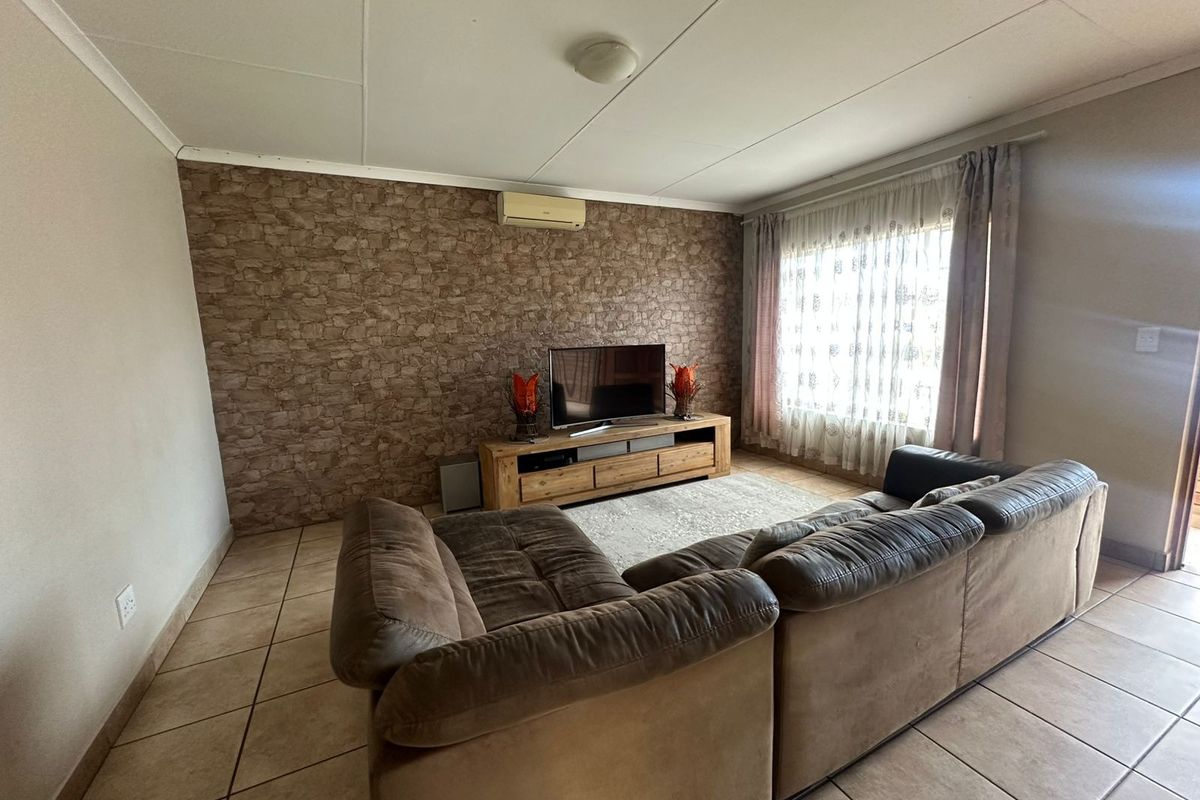 A living room featuring tiled flooring, a textured feature wall, and a wall-mounted split-system air conditioner.