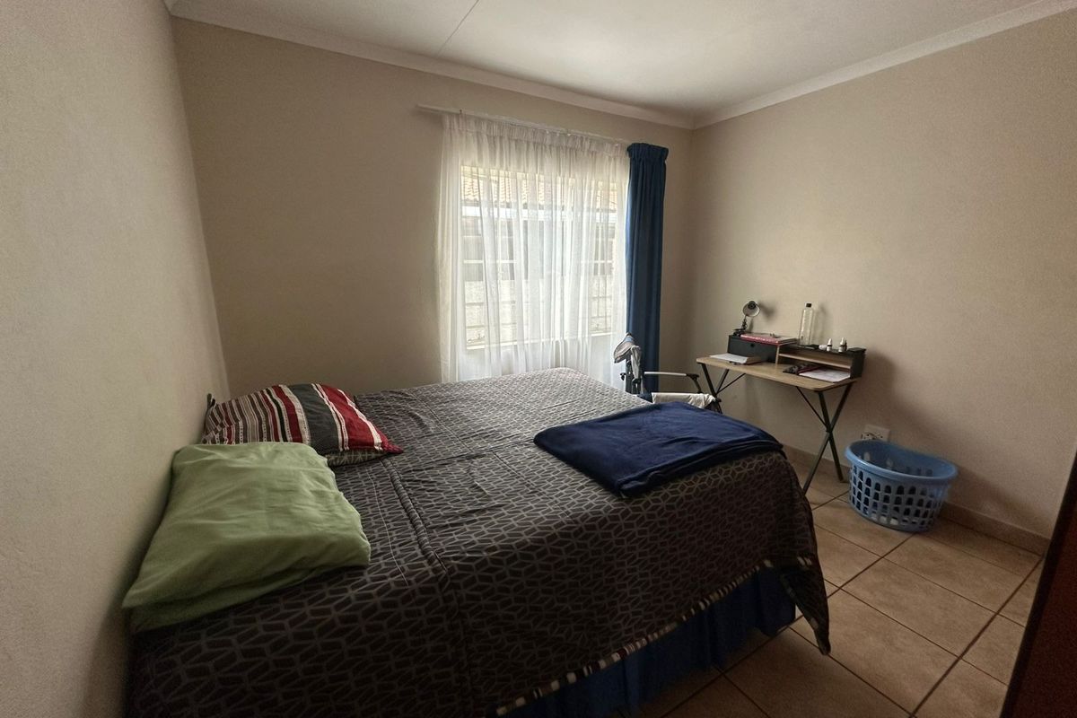 A functional bedroom featuring tiled flooring and a window with curtain rod, offering a neutral space ready for personalization.
