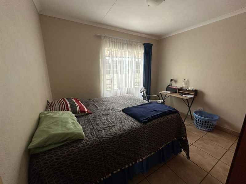 A functional bedroom featuring tiled flooring and a window with curtain rod, offering a neutral space ready for personalization.