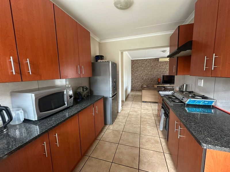 A functional kitchen featuring wood-finish cabinetry, granite countertops, a gas hob with extractor fan, and tiled flooring, leading into an adjacent living area.