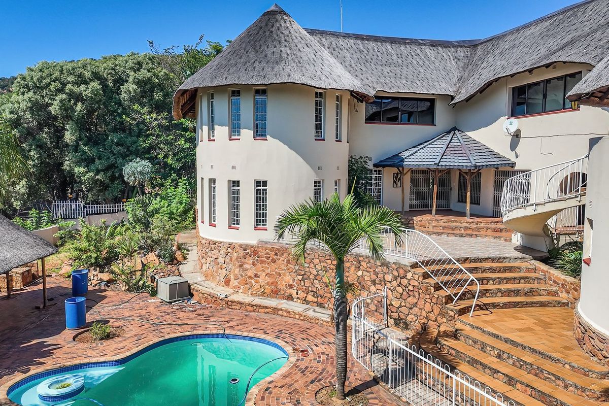 Rear exterior view featuring a swimming pool, stone-clad retaining walls, brick paved patio, and a distinctive thatch roof structure.