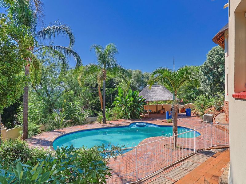 Outdoor pool area featuring a swimming pool, brick paved surround, and a thatched lapa, set within a landscaped garden environment.