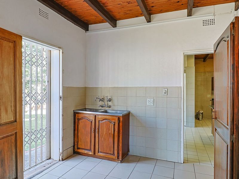 A functional scullery area featuring a double sink, tiled splashback, and exposed timber ceiling beams, with direct access to the exterior.