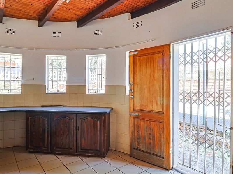 A functional kitchen featuring timber ceiling beams, built-in wooden cabinetry, tiled splashbacks, and direct access to the exterior via a secure door.