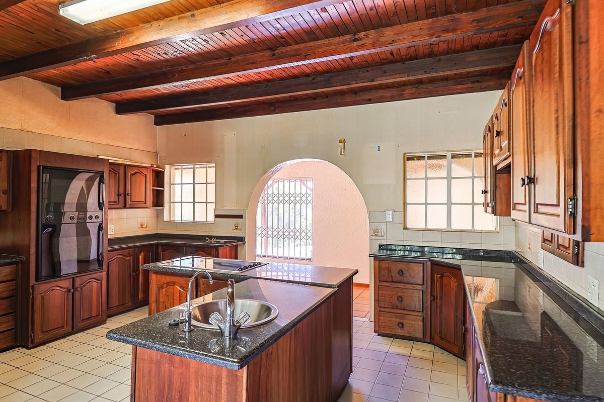 Spacious kitchen featuring timber beam ceilings, granite countertops, built-in wooden cabinetry, and a central island with a double sink.