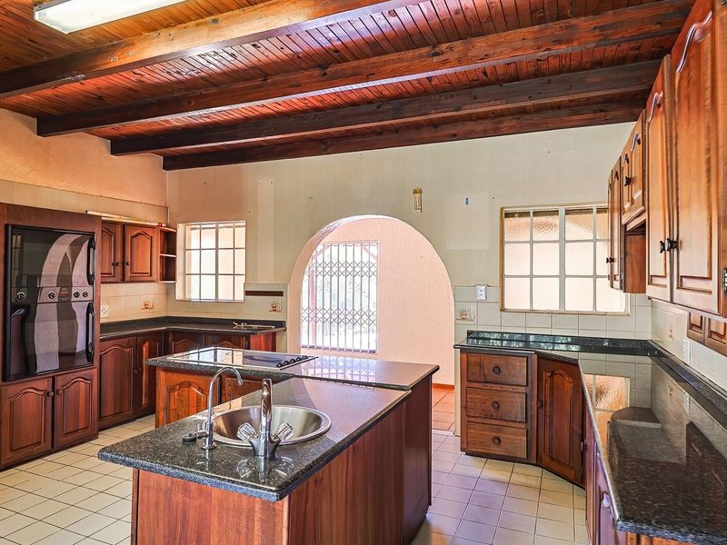 Spacious kitchen featuring timber beam ceilings, granite countertops, built-in wooden cabinetry, and a central island with a double sink.