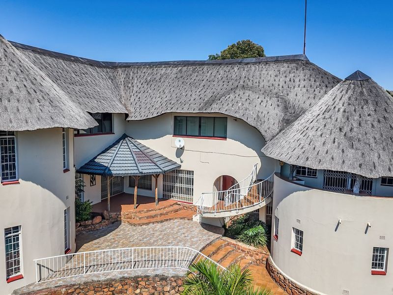 Aerial view of a large residence featuring a distinctive thatched roof, multi-level paved patio areas, and a curved exterior staircase.