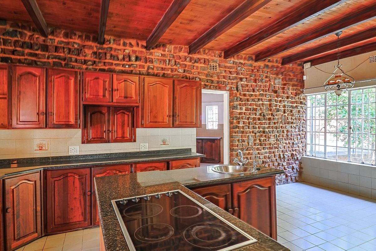 Spacious kitchen featuring rustic exposed brick walls, timber ceiling beams, granite countertops, and ample wooden cabinetry with a central island hob.