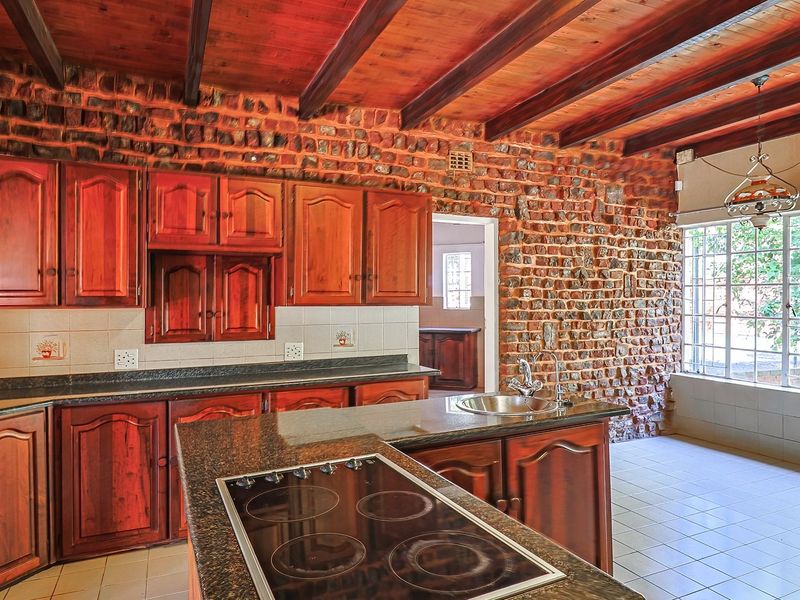 Spacious kitchen featuring rustic exposed brick walls, timber ceiling beams, granite countertops, and ample wooden cabinetry with a central island hob.