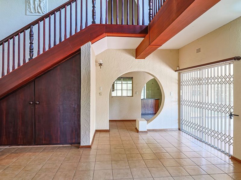 Spacious entrance hall featuring a prominent wooden staircase with under-stair storage, tiled flooring, and an arched architectural opening leading to adjacent living areas.