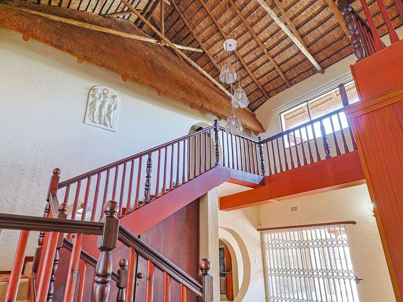 Spacious living area featuring a high vaulted thatched ceiling with exposed timber trusses and a prominent wooden staircase with matching balustrades.