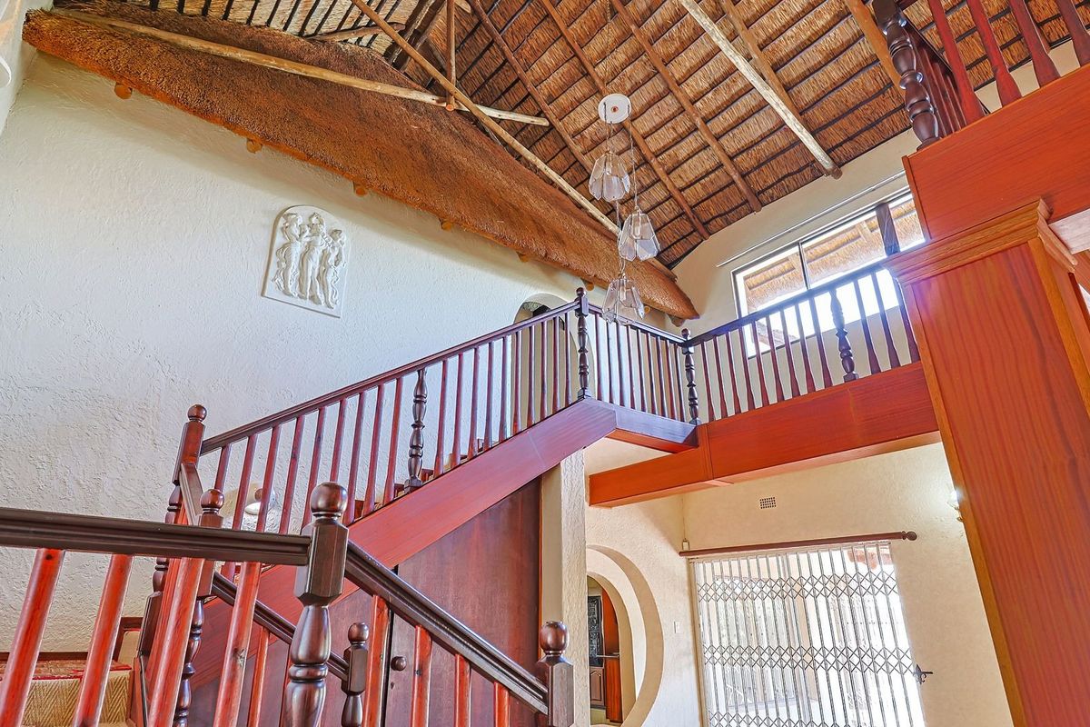 Spacious living area featuring a high vaulted thatched ceiling with exposed timber trusses and a prominent wooden staircase with matching balustrades.