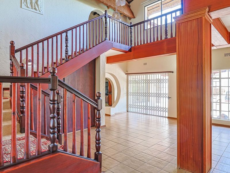 Spacious entrance hall featuring a prominent wooden staircase, tiled flooring, and an arched doorway leading to adjacent living areas.