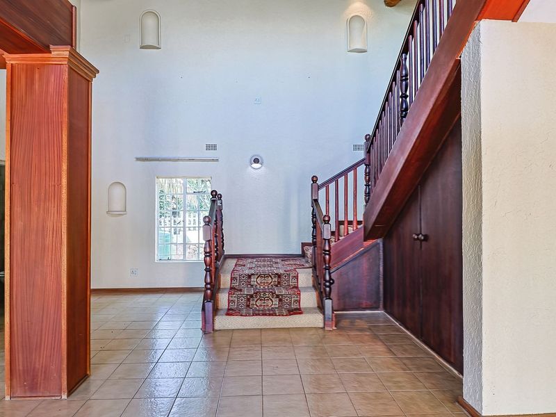 Spacious entrance hall featuring a prominent wooden staircase with built-in storage, tiled flooring, and decorative wall niches.