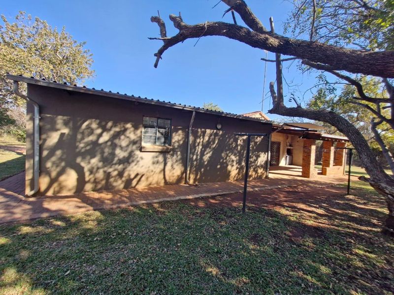 Rear view of the farm dwelling featuring a paved walkway, brick pillars, and a covered patio area under a metal roof.