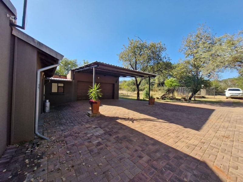 A spacious paved courtyard area featuring a covered carport and double garage access, set within a rural farm property environment.