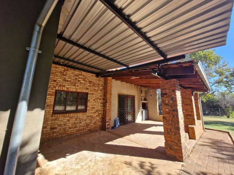 A spacious covered patio featuring exposed brick pillars, a built-in braai, and a corrugated metal roof, offering a functional outdoor entertainment area.