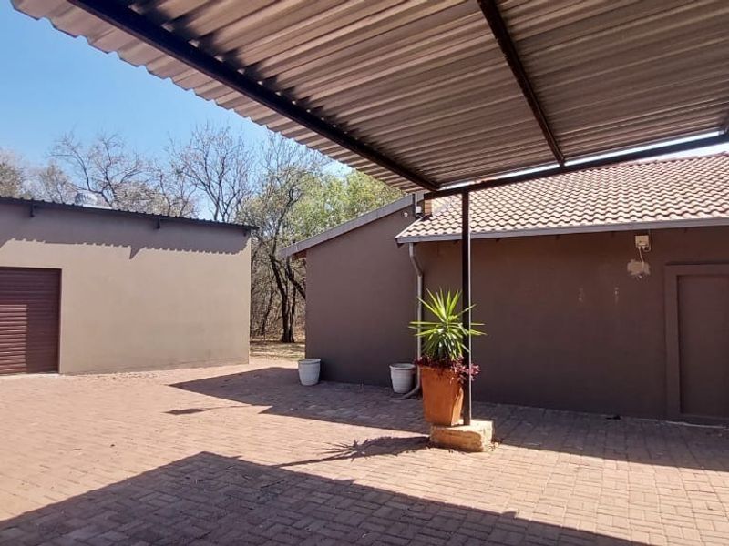 Rear exterior view of the farm property featuring a paved courtyard, covered patio area, and a detached garage structure.