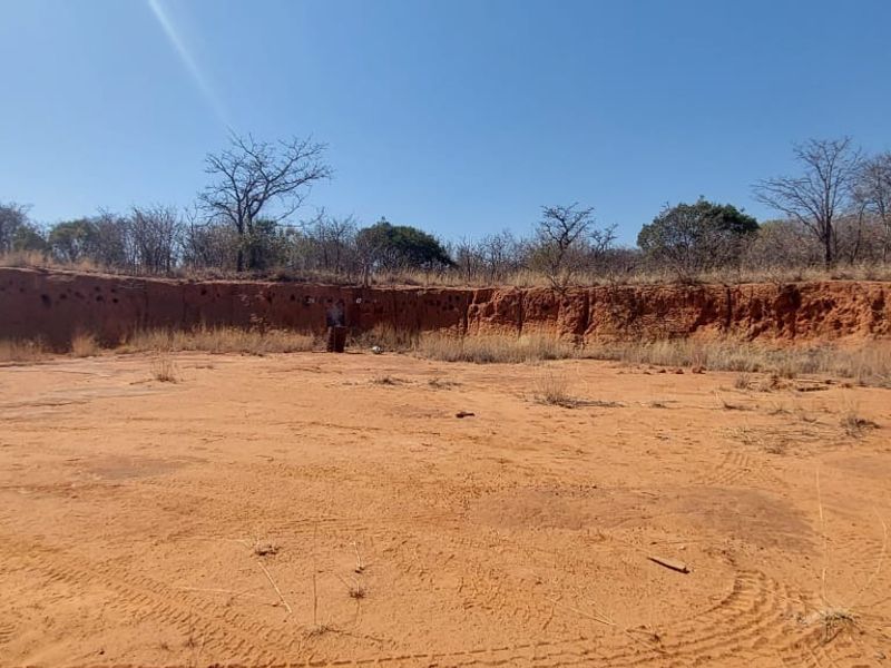 An expansive, cleared area of natural farm land featuring a prominent red earth embankment and surrounding indigenous vegetation.